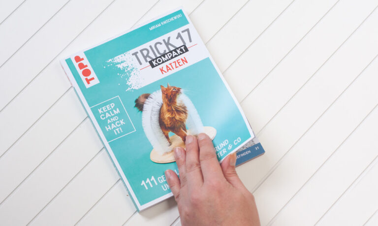 Das Foto zeigt eine Hand, die das Buch Trick 17 kompakt Katzen aufschlägt