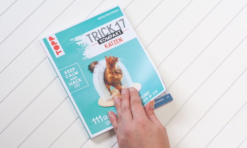 Das Foto zeigt eine Hand, die das Buch Trick 17 kompakt Katzen aufschlägt